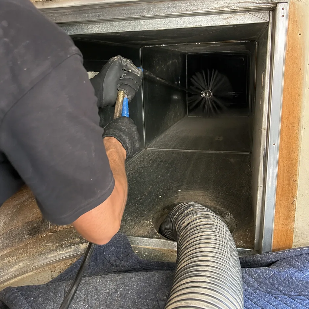 Professional technician performing air duct cleaning with a rotating brush